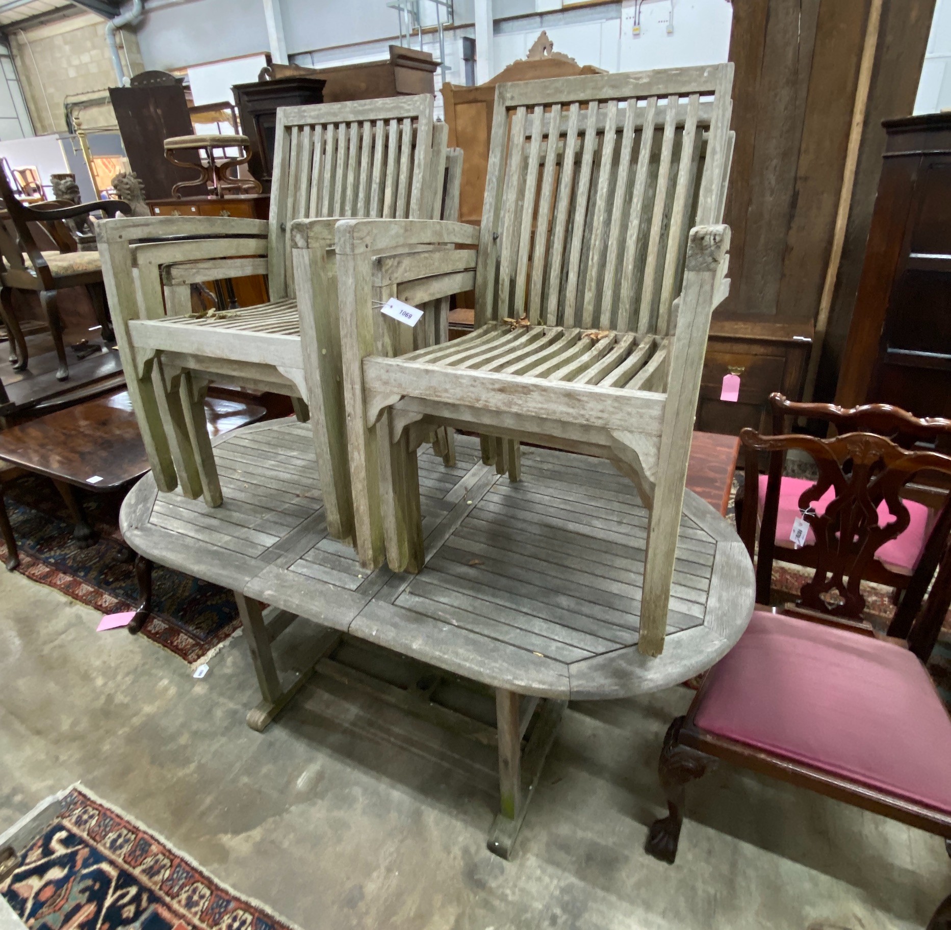 A weathered teak extending garden table, 180cm extended, width 90cm, height 74cm and six stacking chairs